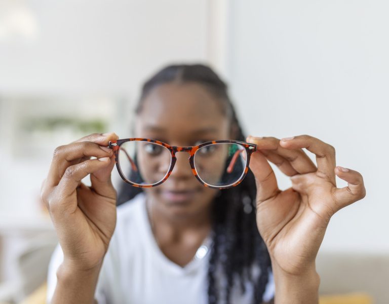 young African woman holds glasses with diopter lenses and looks through them, the problem of myopia, vision correction